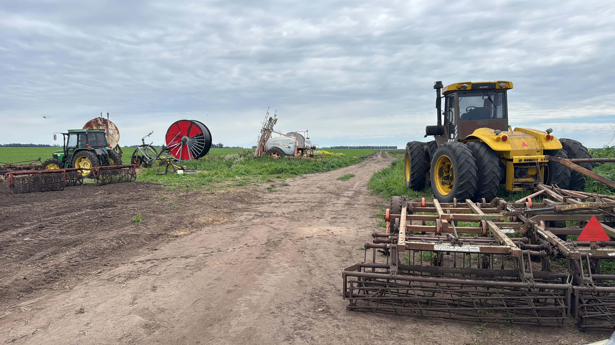 Tractores, rastra y pulverizadora en el campo bajo cielo nublado